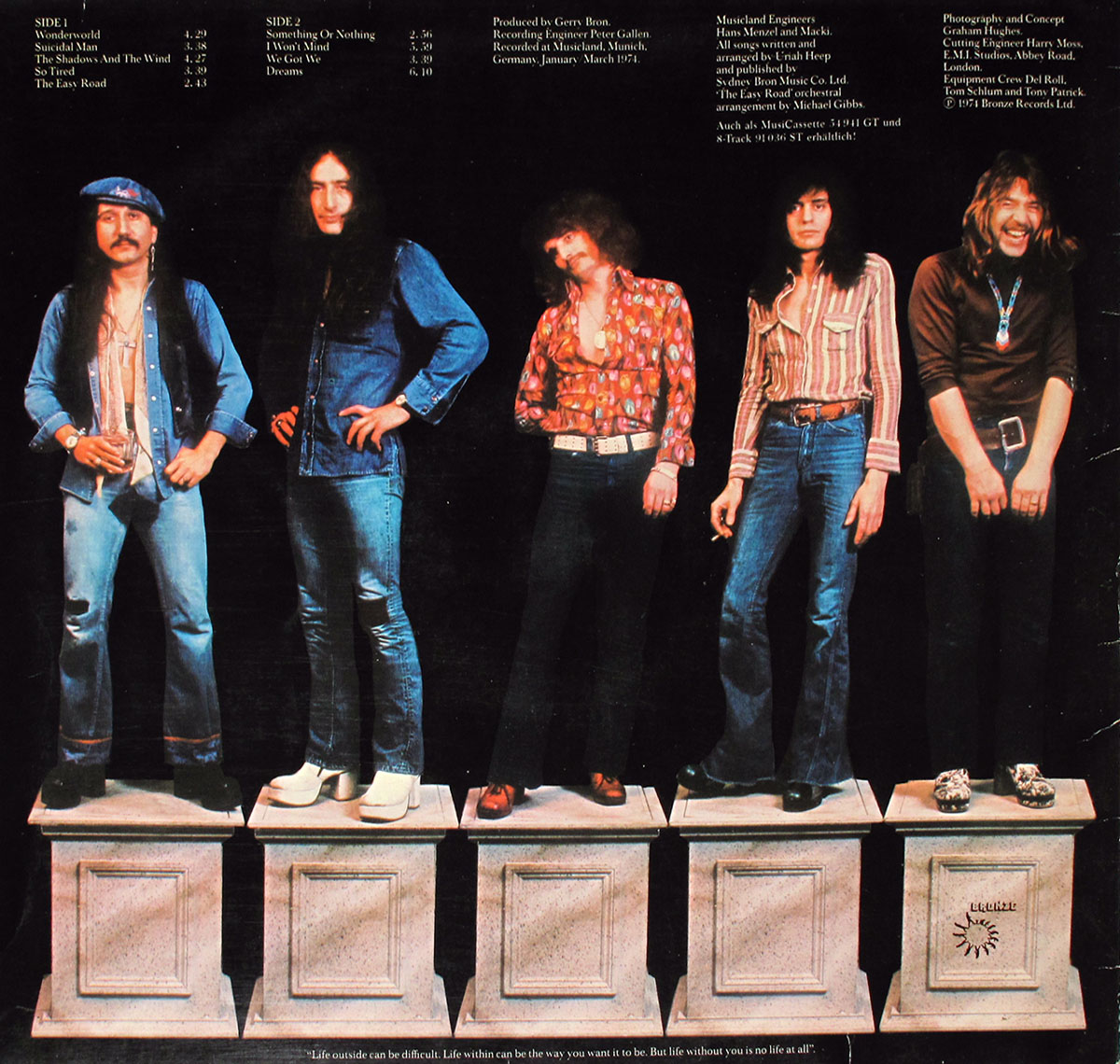 Back cover of Uriah Heep's 'Wonderworld' LP featuring band members standing atop stone pedestals against a black background, dressed in 1970s rock fashion, with tracklist and production credits.